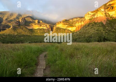 A path leading towards tall sandstone cliffs of the Drakensberg Mountains in the Golden Gate Highlands National Park of South Africa Stock Photo
