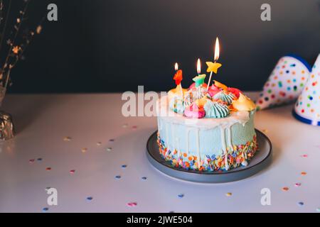 Colorful birthday cake with sprinkles and burning star shaped candles on a dark wall background. Festive birthday celebration, party. Selective focus, Stock Photo
