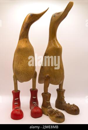 close-up of a pair of carved wooden duck figures wearing coloured lace up boots, white background Stock Photo