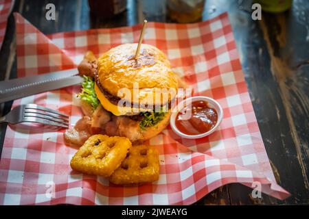 Hamburger set served with hash browns and ketchup on a red and white scotch paper on wooden table looks delicious. Stock Photo