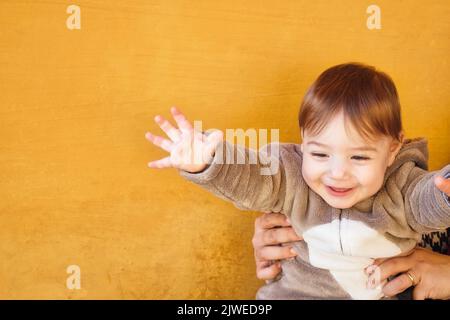 Adorable baby toddler boy wearing a warm winter onesie jumpsuit against a bright orange wall background Stock Photo