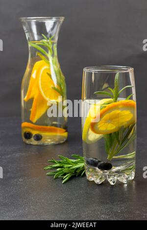 Orange, blueberries and rosemary infused water in glass and bottle. Black background Stock Photo