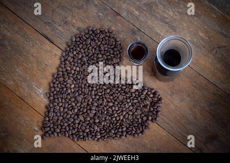Overhead view of roasted coffee beans on a table in a heart shape with a shot of coffee Stock Photo