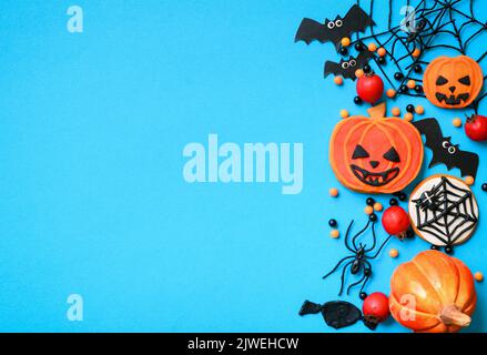Halloween sweets and decorations on blue background. Top view of Halloween cookies, orange pumpkin, spiders, web and bats, and space, flat lay. Concep Stock Photo