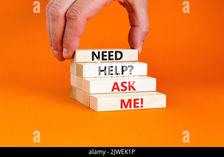 Support and need help ask me symbol. Concept words Need help ask me on wooden blocks on a beautiful orange table orange background. Businessman hand. Stock Photo