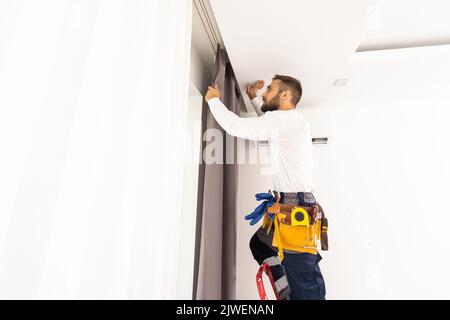 Young man installing curtains over window. Stock Photo