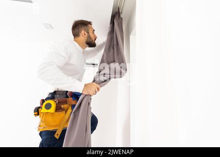 Young man installing curtains over window. Stock Photo