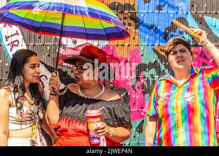 Goiânia, Goias, Brazil – September 05, 2022: Two people talking under the umbrella and another person next to them in colorful clothes, looking up. Stock Photo