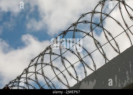 Chain link fence with barbed wire and razor wire. against the blue sky. Stock Photo