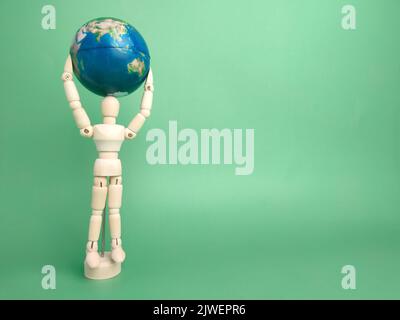 A wooden mannequin holding earth globe on green background with copy space. Stock Photo