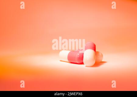 Three red white pill capsules in a slide on an orange background with a gradient. Pharmacy and medicine theme. Stock Photo