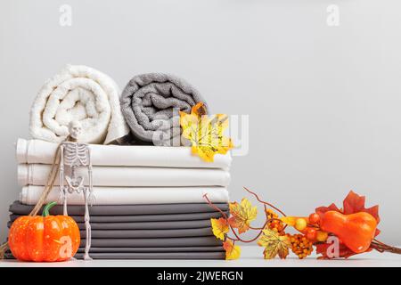 A stack of bed linen, a bed sheet and folded rolls of towels on a table with Halloween decor. Stock Photo