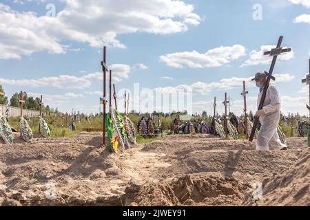 A man in a protective suit carries a funeral cross to a fresh grave. Burial of the remains of 13 unidentified and two identified people who were killed in the Buchan district during the Russian occupation, on September 2, 2022. A few months after the de-occupation of the Bucha district, those bodies that were not identified were buried and marked with numbers at the cemetery in Bucha. According to the deputy mayor of Buch Mykhailyna Skoryk, a total of 419 people who were killed during the Russian occupation of the Buchan district were buried in the city. (Photo by Mykhaylo Palinchak/SOPA Ima Stock Photo