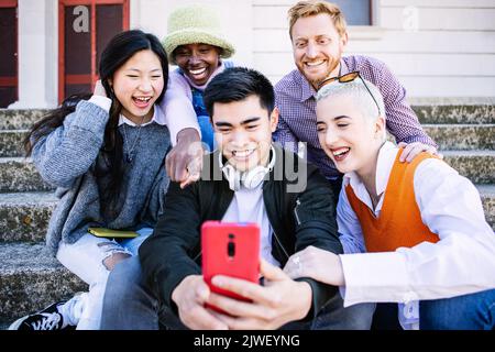 Happy group of young people having fun using mobile phone together outdoors Stock Photo