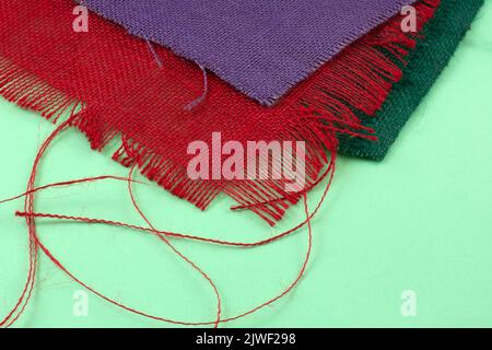 Frayed green, red and purple burlap fabric pieces on light green background Stock Photo