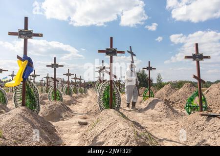 Bucha, Ukraine. 2nd Sep, 2022. A man in a protective suit carries a funeral cross to a fresh grave. Burial of the remains of 13 unidentified and two identified people who were killed in the Buchan district during the Russian occupation, on September 2, 2022. A few months after the de-occupation of the Bucha district, those bodies that were not identified were buried and marked with numbers at the cemetery in Bucha. According to the deputy mayor of Buch Mykhailyna Skoryk, a total of 419 people who were killed during the Russian occupation of the Buchan district were buried in the city. (Cre Stock Photo