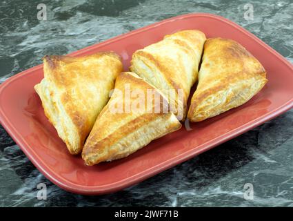Baked breakfast apple turnover pastries on red serving plate on table Stock Photo