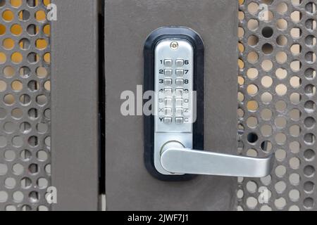 Locked private metal security gate door with push button combination lock system keypad with metallic silver doorknob handle Stock Photo