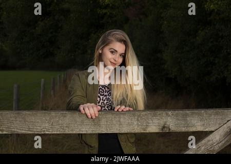 A beautiful blonde teenager leaning on a gate Stock Photo