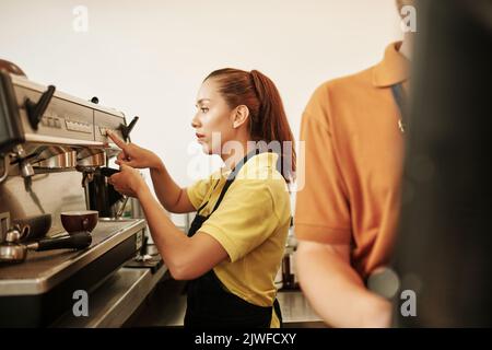 New coffeeshop barista pushing button on coffee machine when making cappuccino for customer Stock Photo