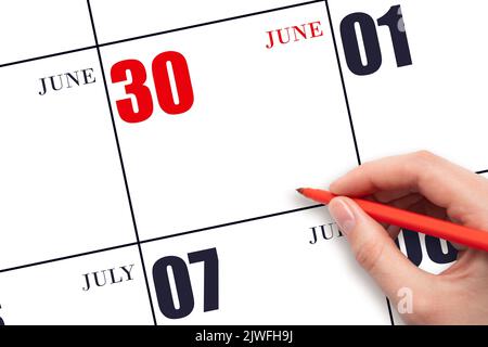 30th day of June. A hand holding a red pen and pointing on the calendar date June 30. Red calendar date, copy space, mockup. Summer month, day of the Stock Photo