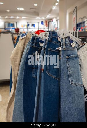 Many jeans hanging on a rack. Row of pants denim jeans hanging in closet, concept of buy and sell. Jeans on the hangers on a sale in Old Navy Store-Au Stock Photo
