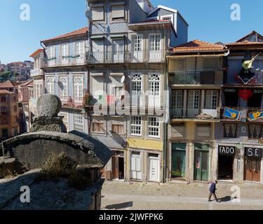 Traditional Porto buildings with balconies as an elderly man walks along the street. A Fado show venue with guitars outside is on the right. Stock Photo