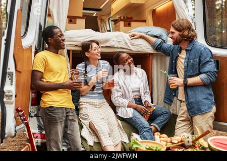 Group of friends drinking cocktails and talking to each other during camping on motorhome Stock Photo