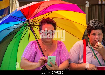 Goiânia, Goias, Brazil – September 05, 2022:A woman holding an umbrella and using a cell phone next to another woman talking into the cell. Stock Photo