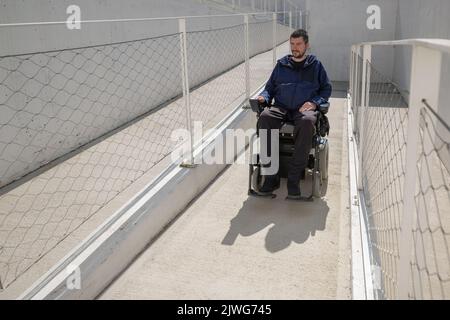 Man in a wheelchair use an accessible ramp. Stock Photo