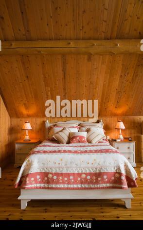 King size bed in master bedroom on upstairs floor inside handcrafted spruce log home. Stock Photo