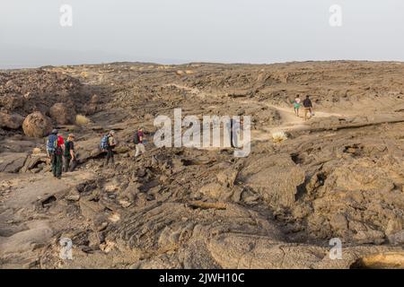 AFAR, ETHIOPIA - MARCH 26, 2019: Tourists walking across lava fields at Erta Ale volcano in Afar depression, Ethiopia Stock Photo