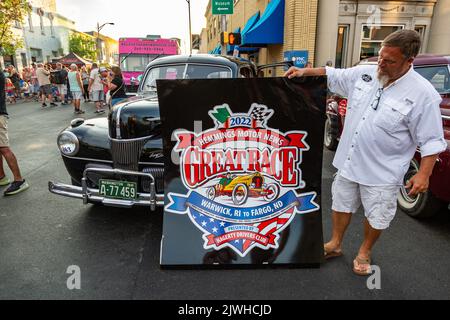 At the ACD Festival, man holds a sign advertising the 2022 Hemmings Motor News Great Race. The black 1941 Ford Super Deluxe behind him participated. Stock Photo
