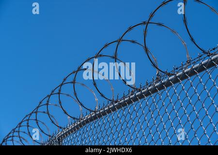 Fence with razor wire with blue sky in background. Stock Photo