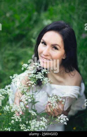 A woman in a white dress surrounded by nature and white flowers of Aegopodium podagraria. Vertical photo. Stock Photo