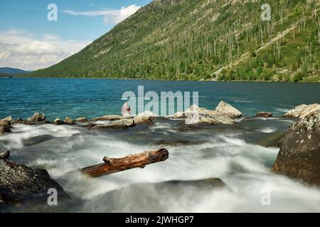 A boy seen sitting near Siberian cedar on the 'Shumy' of the Multa River in the Altai Mountains.Just four hours by plane from Moscow, and you find yourself in a completely different world: the world of majestic young mountains, wide green hilly valleys, cedar forests, turbulent rivers and glacial lakes. Altai! Stock Photo