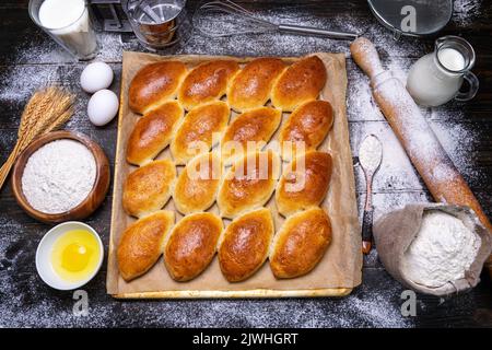 making homemade pies. Top view of baking sheet with homemade pies, rolling pin flour eggs and baking ingredients Stock Photo
