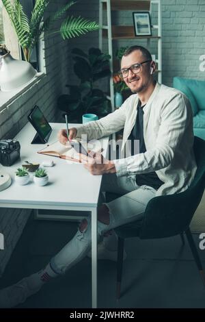 Portrait of a smiling handsome young man wearing eyeglasses checking his phone, planning projects, and making notes in a diary. Internet technology Stock Photo