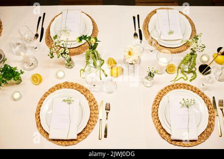 Top view of part of served dinner table with plates, napkins, wineglasses, lemons, flowers and candles prepared for wedding party Stock Photo