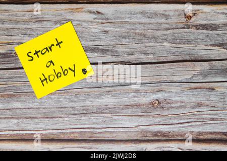 Start a hobby for a healthy lifestyle and wellbeing concept. Yellow sticky note reminder in wooden background with copy space. Stock Photo