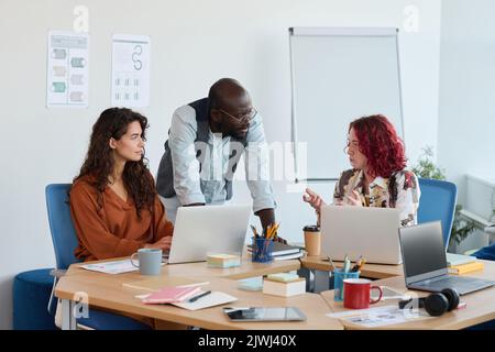 Two intercultural managers listening to their female colleague explaining her idea for new business project during discussion at meeting Stock Photo