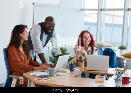 Three young multicultural employees laughing at working meeting in office during discussion of new ideas or points of project Stock Photo