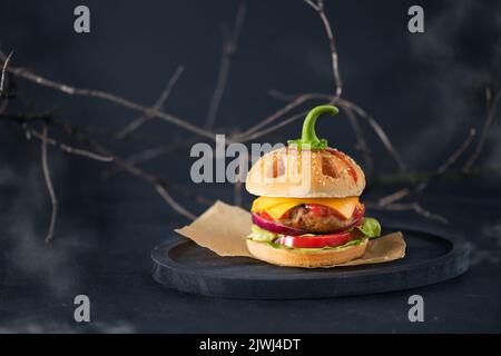 Halloween burger in a shape of pumpkin head jack o lantern on black. Scary cheeseburger on halloween party. Stock Photo