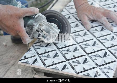 Tiling a bathroom. A man is cutting a bathroom ceramic tile with a disc angle grinder. Stock Photo
