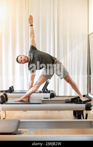 Male athlete practicing pilates on reformer in exercise room Stock