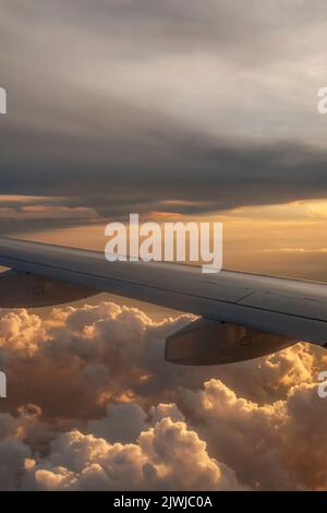 Vertical view of an airplane flying above the clouds against a beautiful sunset Stock Photo