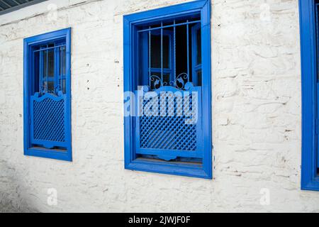 Blue window shutters on a white house. Wooden windows with closed shutters. Shutters on the windows protect from sunlight Stock Photo
