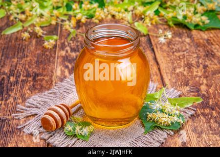 A jar of honey, a honey stick and linden flowers on an old board. rustic concept Stock Photo