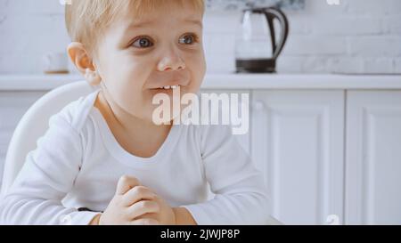 cheerful toddler boy sitting in feeding chair while looking away at home Stock Photo
