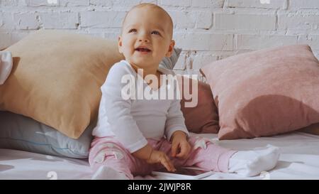 happy toddler child sitting on bed with smartphone around pillows Stock Photo